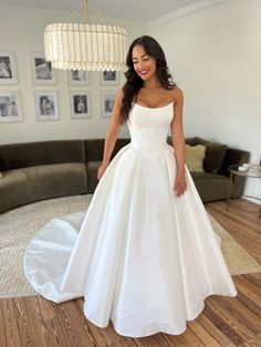 a woman in a white wedding dress standing on a wooden floor next to a couch