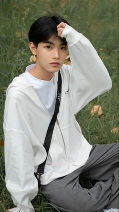 a young man sitting in the grass wearing a white shirt and black suspender tie