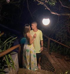 a man and woman standing on steps in the woods at night, one holding his hand up to her chest