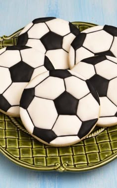 three cookies decorated with black and white soccer balls on a green plate, sitting on a blue surface