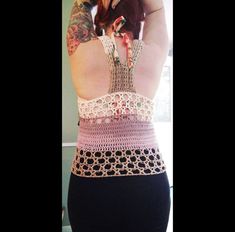 a woman with tattoos on her arms and back, wearing a tank top that is crocheted