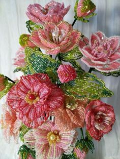 pink flowers with green leaves and beads in a vase on a white cloth covered table