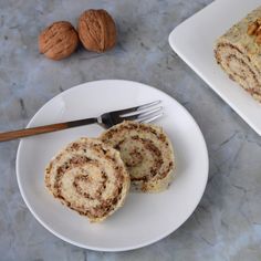 two pieces of cinnamon roll sitting on top of a white plate next to walnuts