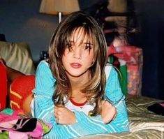 a young woman laying on top of a bed next to a pile of clothes and toys