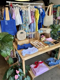 a wooden table topped with lots of different types of clothing and accessories next to potted plants