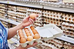 a person holding a carton of eggs in front of shelves with eggs on them