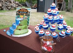 a table topped with cupcakes and cakes covered in frosting next to a sign