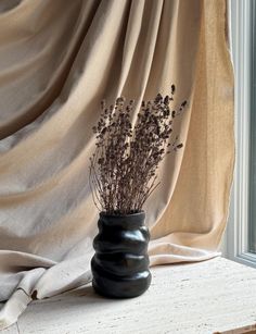 a black vase sitting on top of a window sill next to a white curtain