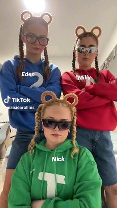 three girls wearing mickey mouse ears and sweatshirts, one with her arms crossed while the other wears sunglasses