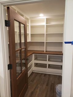 an empty walk in closet with white shelves and wood doors, next to a trash can