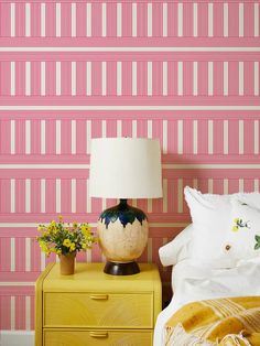 a bedroom with pink and white striped wallpaper next to a yellow nightstand topped with flowers