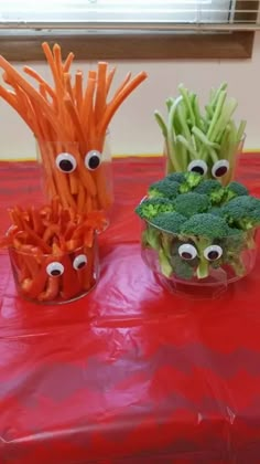 carrots and broccoli with googly eyes are on a red tablecloth