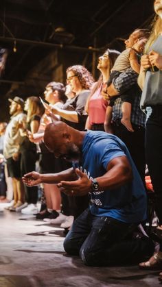 a man kneeling down in front of a group of people who are standing and clapping