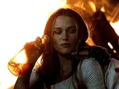 a woman drinking from a bottle while standing in front of a fire with her eyes closed