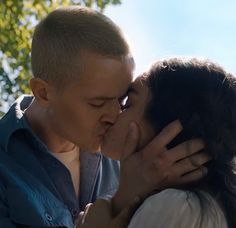 a man and woman kissing each other in front of some trees on a sunny day