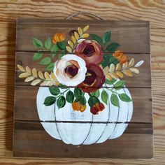 a painted pumpkin with flowers in it sitting on a wooden table next to wood planks