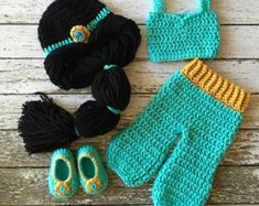 a crocheted baby outfit, booties and hat on a wooden surface with yarn