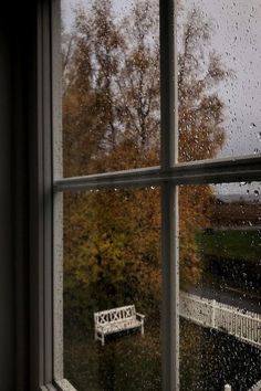 a window with rain falling on it and a bench in the foreground