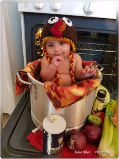 a baby in a turkey costume sitting in an oven next to vegetables and other foods