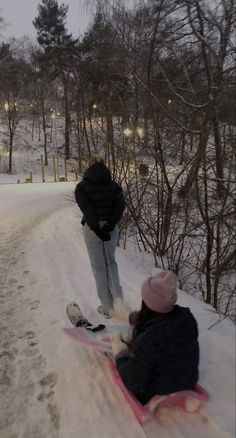 two people sitting in the snow on sleds and one person standing next to them