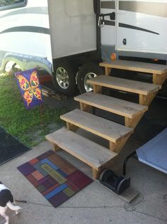 a dog is standing next to some stairs and a camper in the back ground