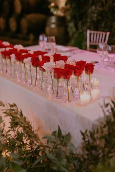 a long table with candles and red roses in vases on it's side