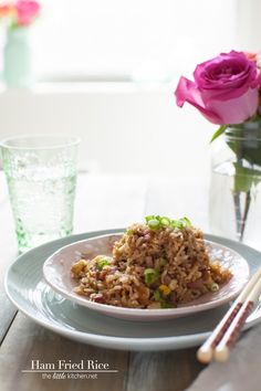 rice and vegetables on a plate with chopsticks in front of the plate, next to a pink rose