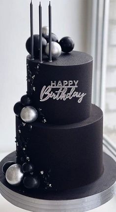 a three tiered black cake with candles on top and happy birthday written on it