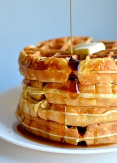 a stack of waffles with syrup being drizzled over them on a white plate