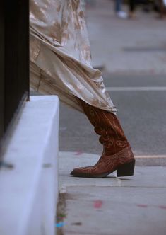 a person in cowboy boots is standing on the sidewalk with their leg up against a wall