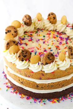 a cake with white frosting and colorful sprinkles on the top is topped with chocolate chip cookies