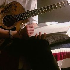 a person sitting on a bed holding a guitar and writing something in a notebook with an american flag pillow behind them