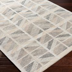 a white rug with grey and beige squares on top of wooden flooring in an area that has dark wood floors