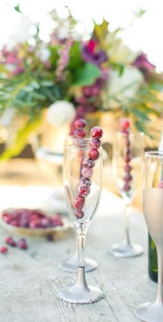 three wine glasses sitting on top of a wooden table next to bottles and vases