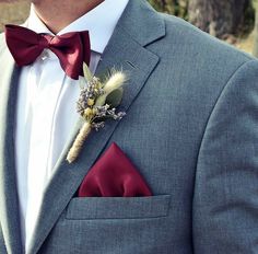 a man wearing a gray suit with a red bow tie and boutonniere