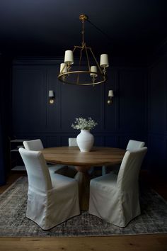 a dining room table with white chairs and a chandelier hanging from the ceiling