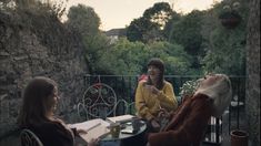 three women sitting at an outdoor table talking to each other and one woman holding a coffee cup