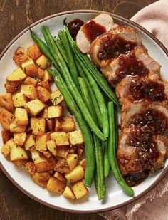 a white plate topped with meat and green beans next to potatoes on a wooden table