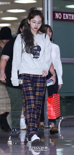 the young woman is wearing plaid pants and a white sweatshirt, while walking through an airport