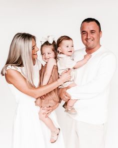 a man, woman and child are posing for a family photo in white outfits with their arms around each other