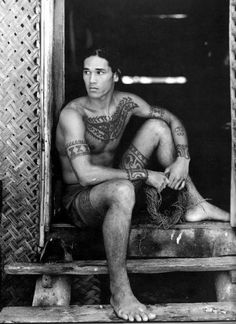 an old photo of a man with tattoos on his arms and legs sitting in a doorway