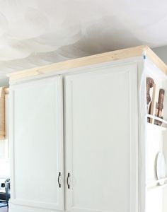 a kitchen with white cupboards and wooden shelves on the wall above it is an unfinished ceiling