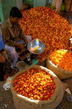 two men sitting in front of bags filled with oranges and other items on the ground