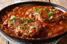 some meatballs and sauce in a black pan on a wooden table with a checkered napkin