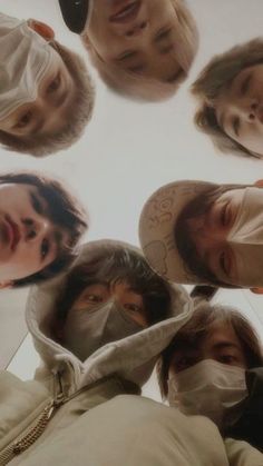 five people wearing face masks in a circle looking up at the camera with their heads covered