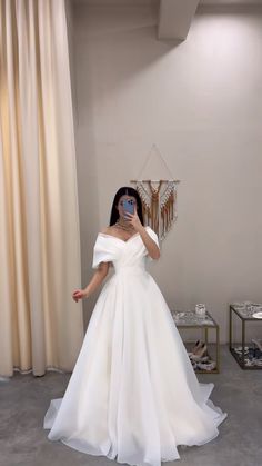 a woman in a white dress taking a selfie with her cell phone while wearing an off the shoulder wedding dress