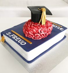 a graduation cake made to look like a brain on top of a book with a mortar and tassel