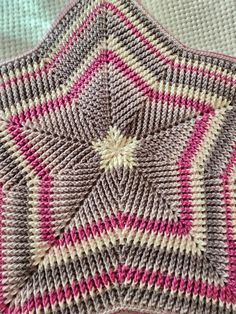 a crocheted blanket with pink and white designs on it's edges, in the shape of a star