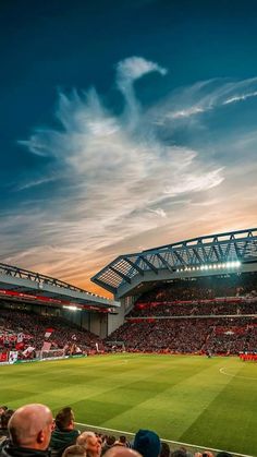 a stadium filled with lots of people sitting on top of a soccer field at sunset