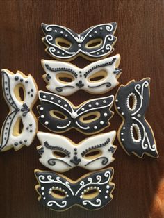 decorated sugar cookies with black and white masks on wooden table top next to each other